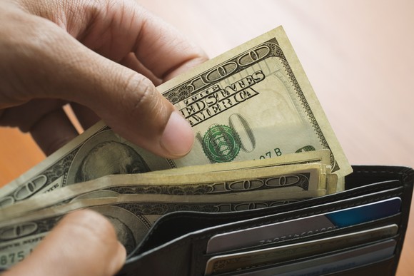 A person pulling four one hundred dollar bills out of an open wallet. 