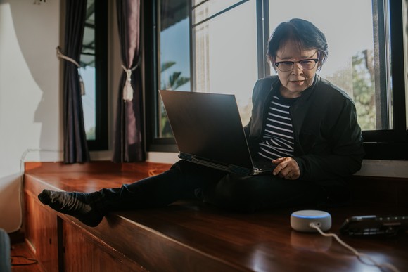 Adult sitting on windowsill looking at computer.