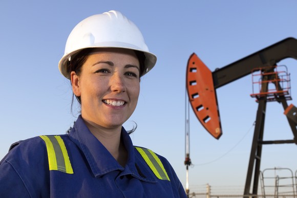 A person in protective gear with an oil well in the background.