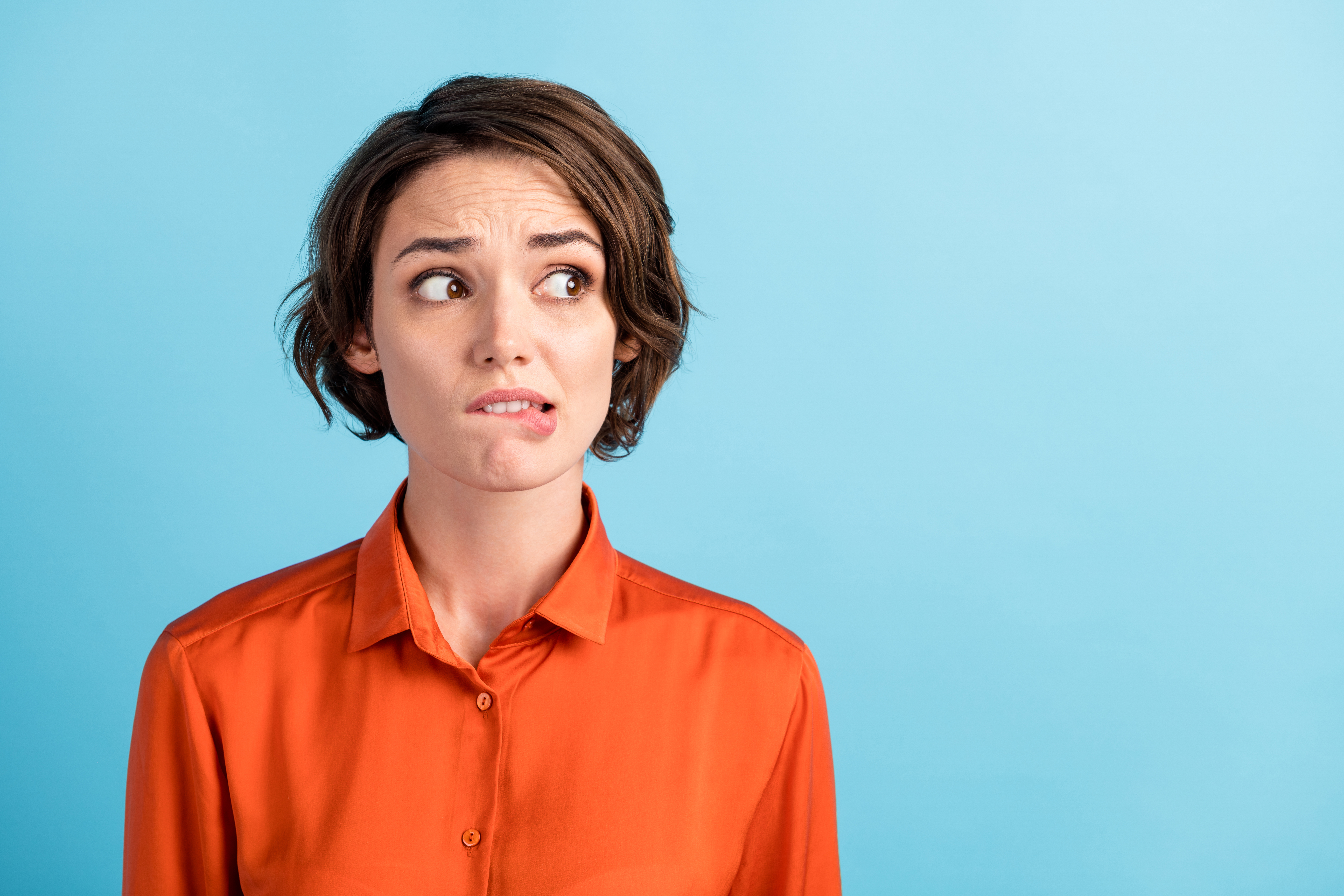 A person in an orange shirt bites their lip.