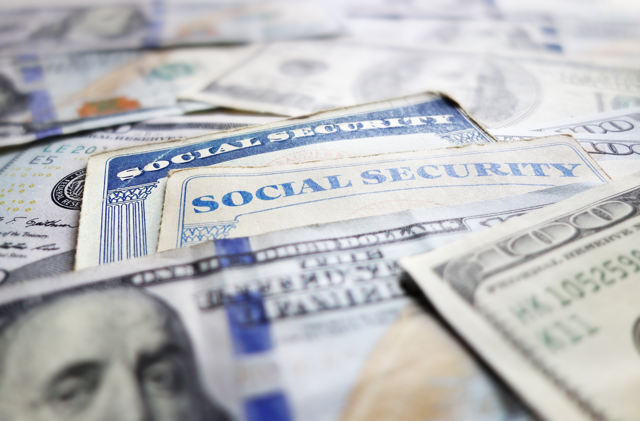 Two Social Security cards placed atop a messy pile of one hundred dollar bills.