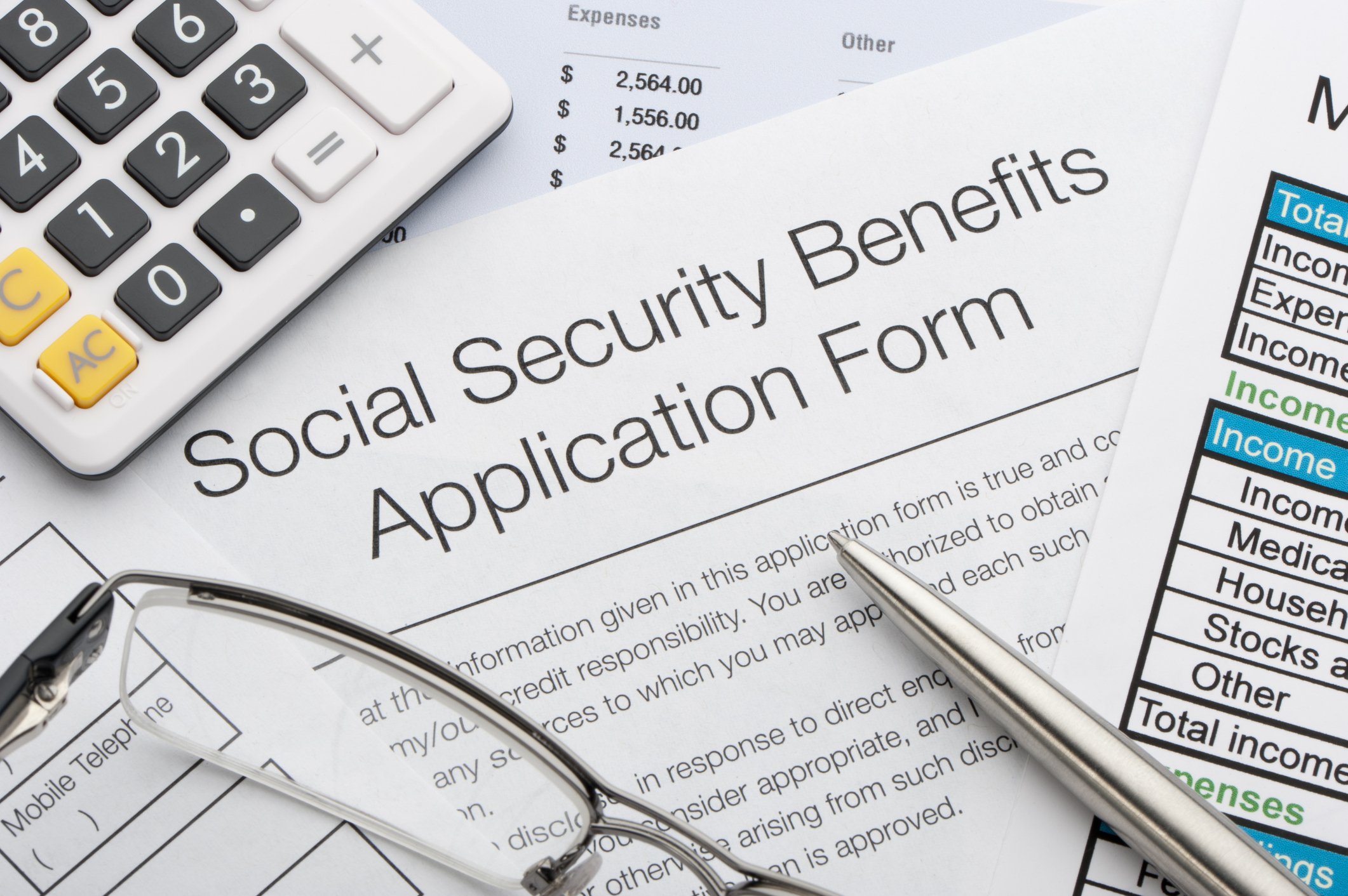 A Social Security benefits application form amid scattered papers, a calculator, a pen, and glasses.