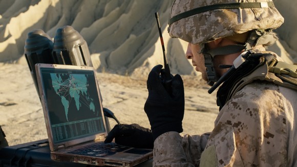 A soldier uses a laptop on the field.