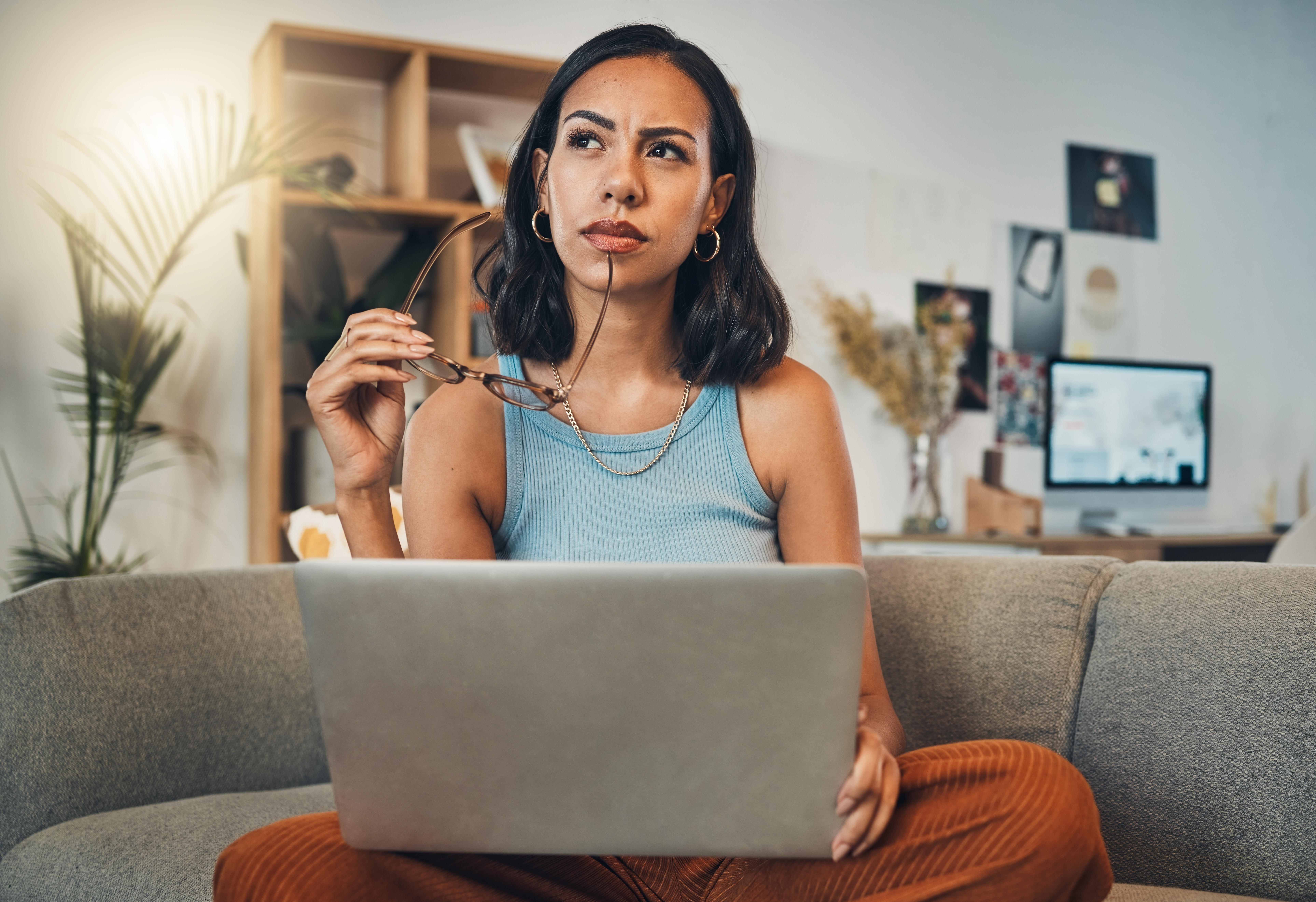A person on a couch holding a pair of eyeglasses with a laptop in their lap.