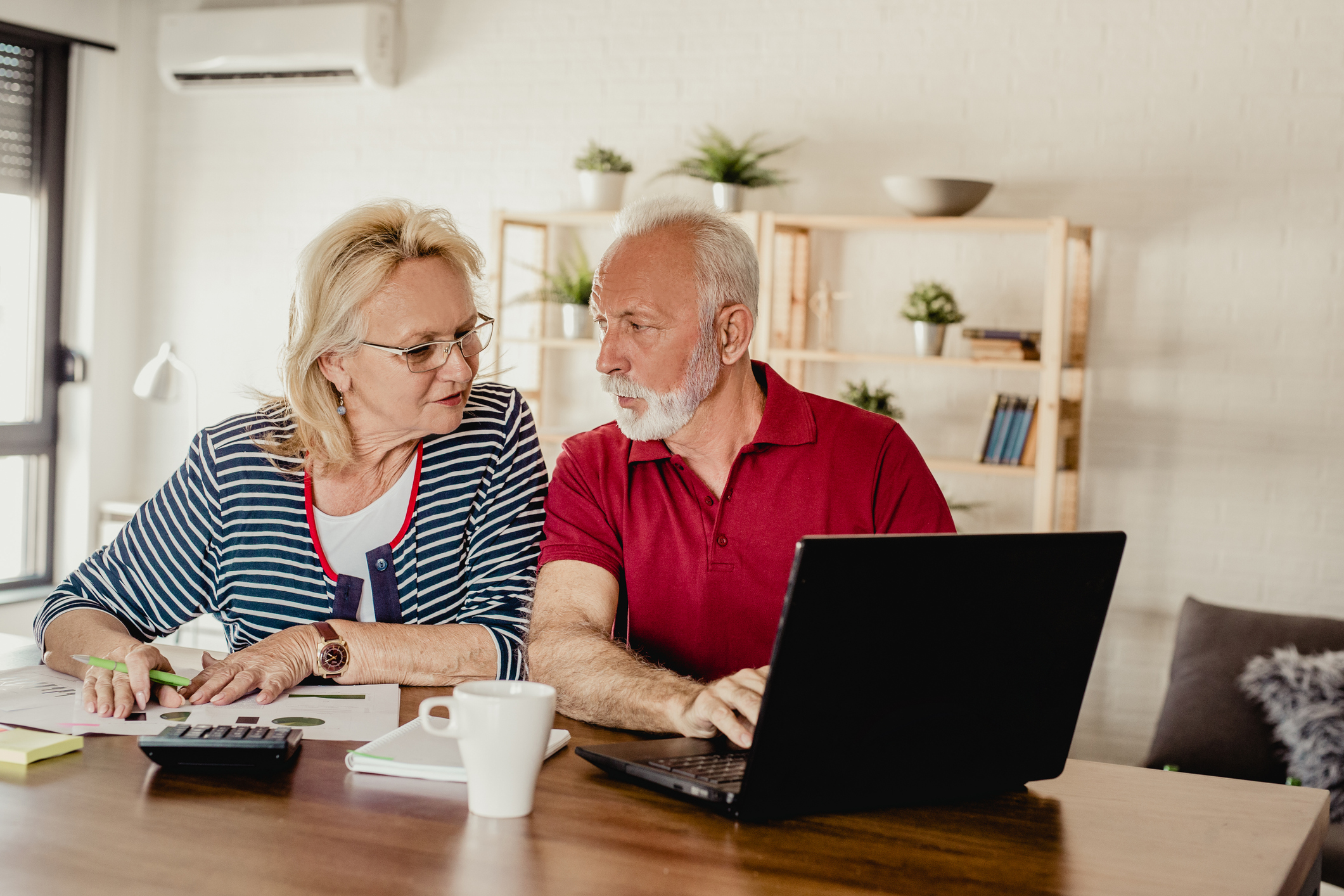 Two seniors sitting at a table with a laptop and calculator.