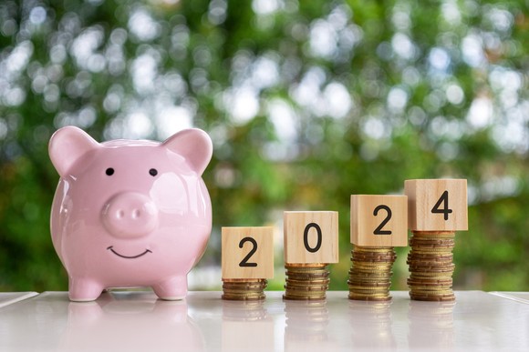 A piggy bank next to a stack of coins with wooden blocks that spell 2024. 