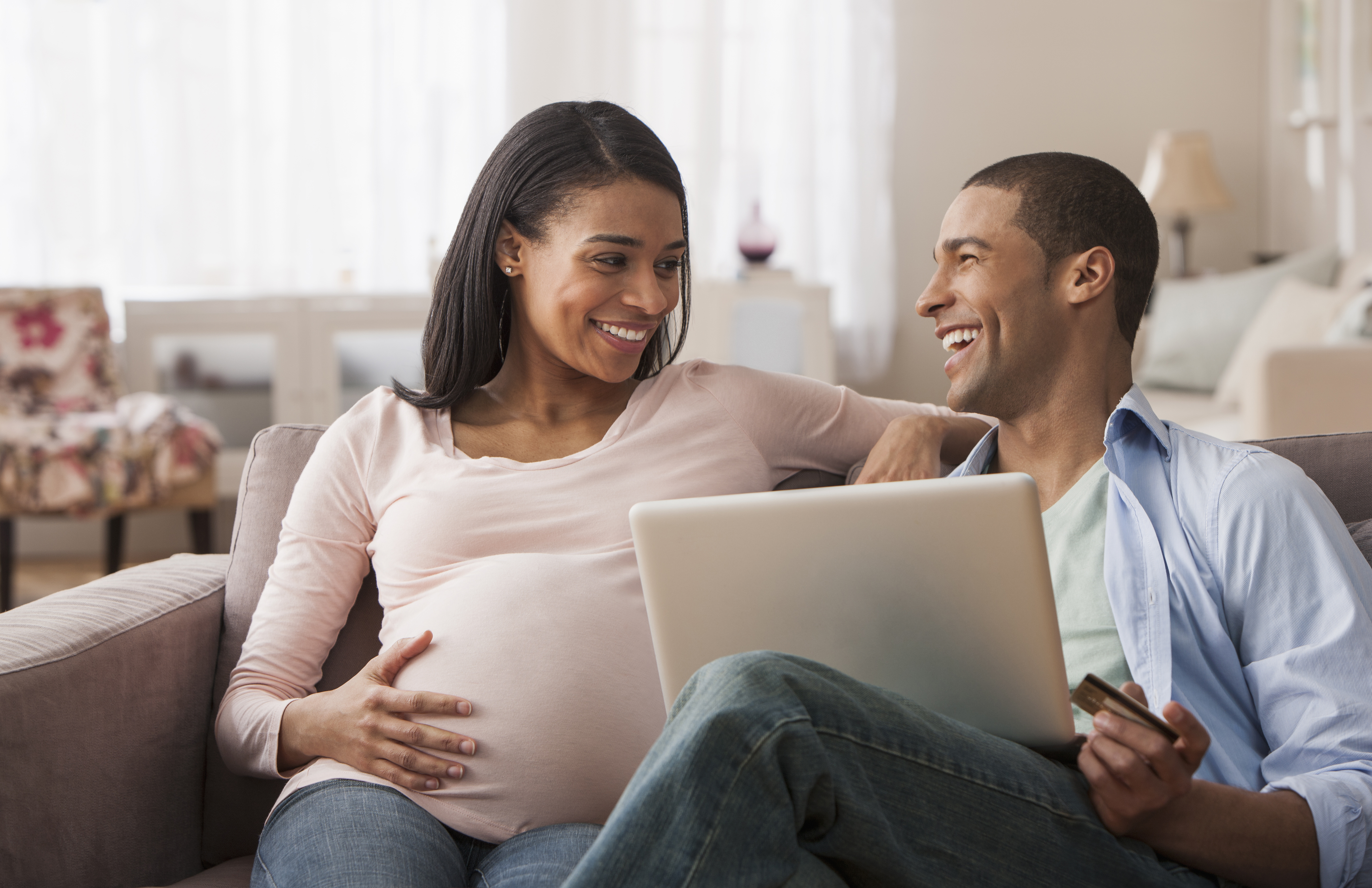 A smiling couple sitting together on a couch using a laptop.