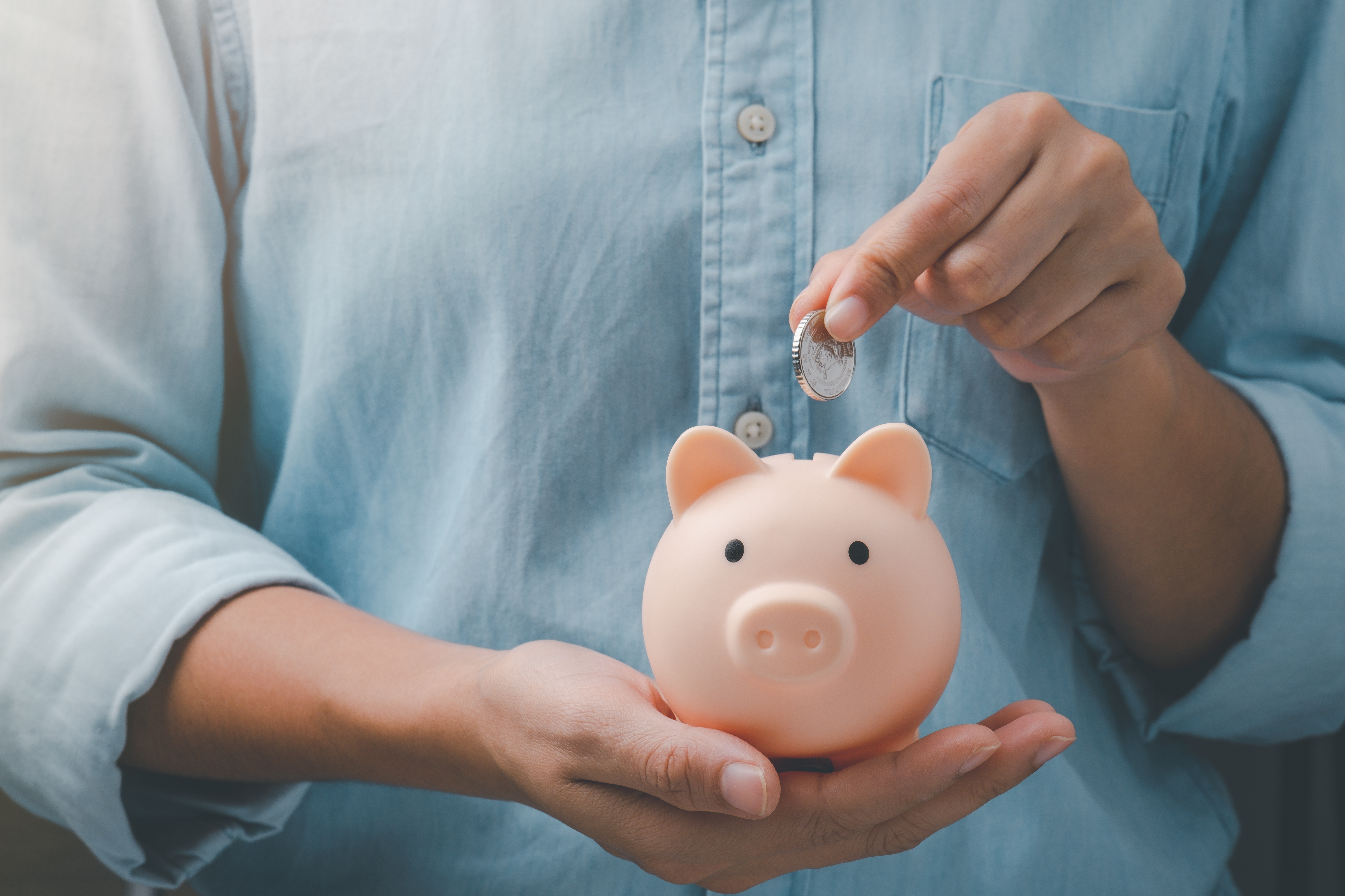 Someone inserting a coin into a piggy bank.