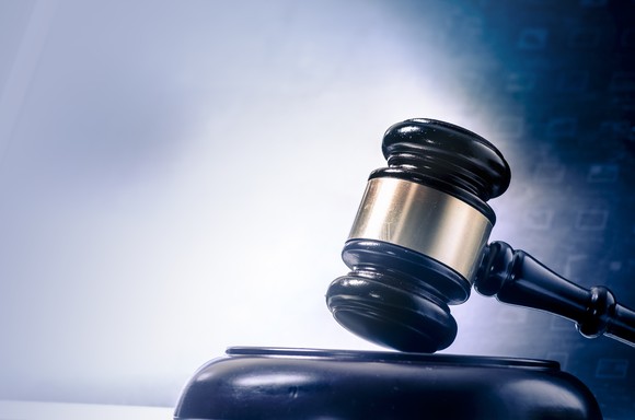 A judge's gavel rests on a wooden stand with digital numbers floating in the background.