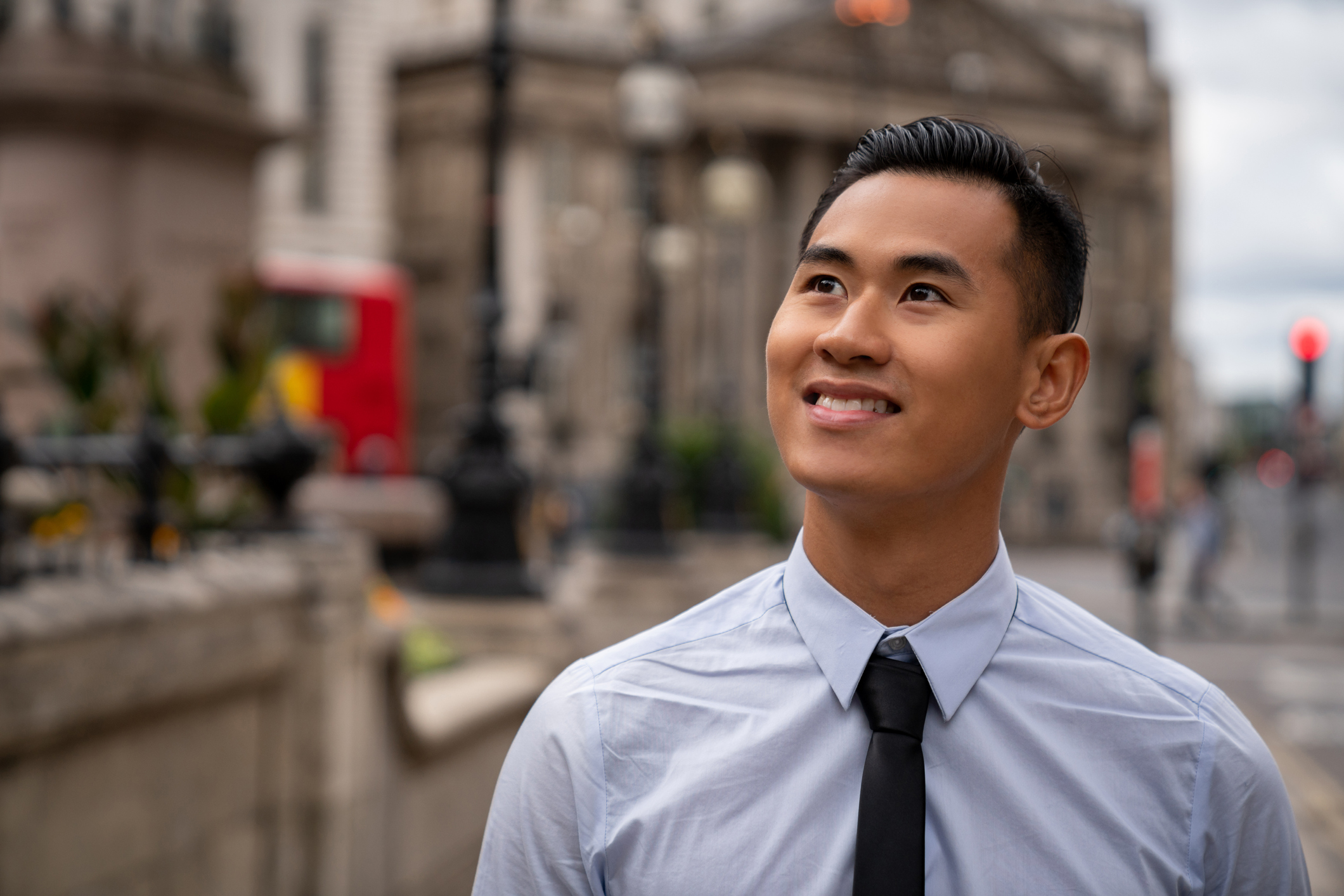 An investor on a city street smiles while looking up at the sky.