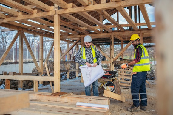 Two people wearing personal protective equipment work on building a house. 