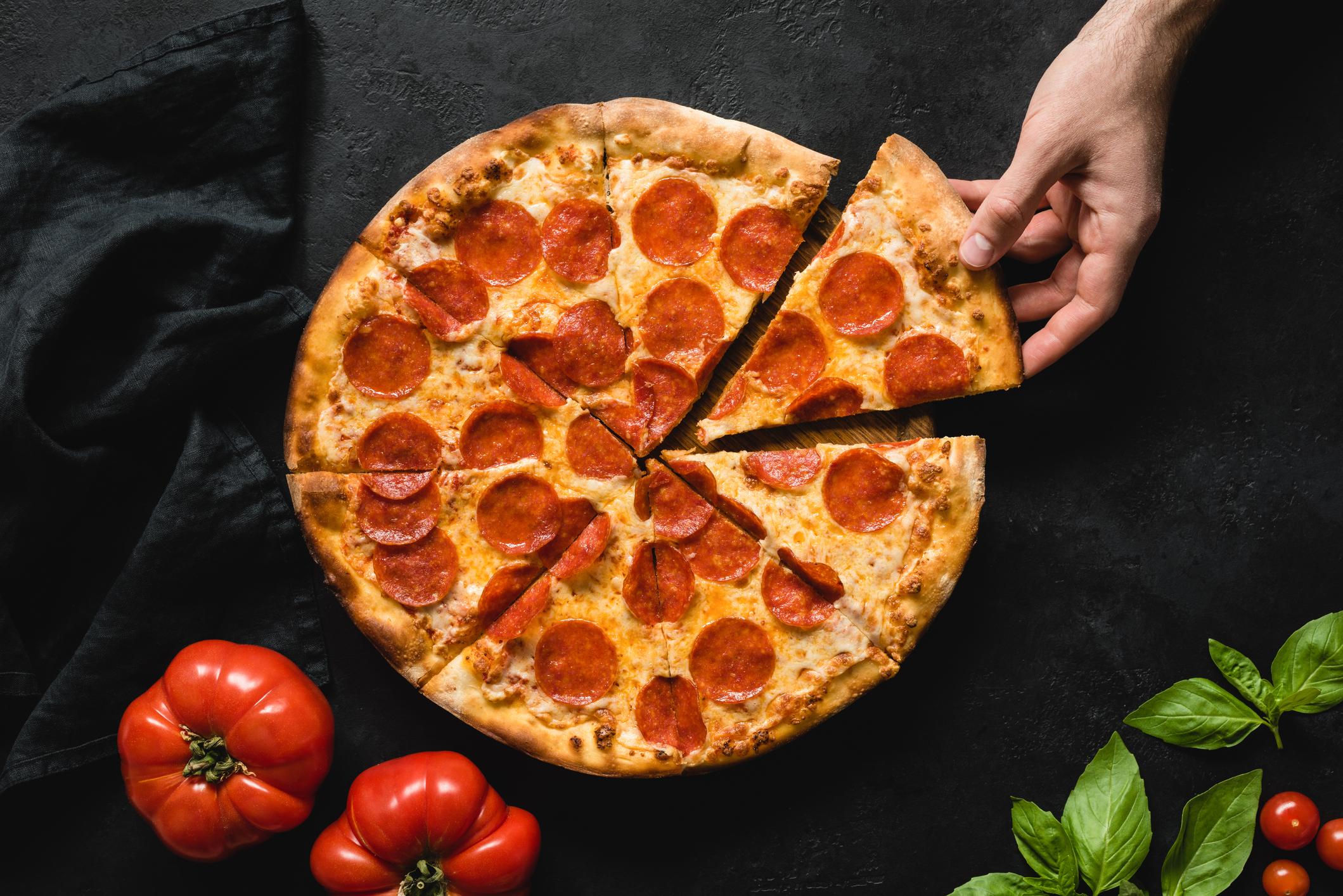 Someone taking a slice from a pizza cut into eight sections.