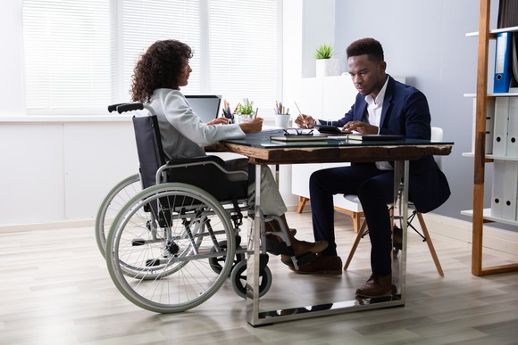Two people sitting across a table from each other holding writing utensils and looking at documents.