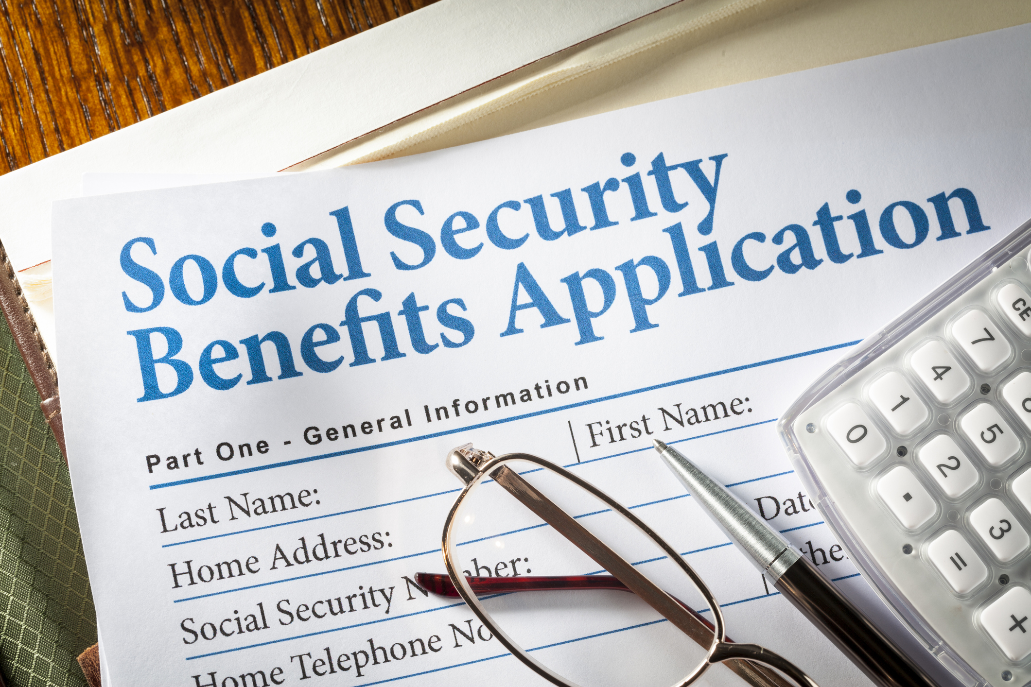 A pair of glasses, a pen, and a calculator set atop a Social Security benefits application form.