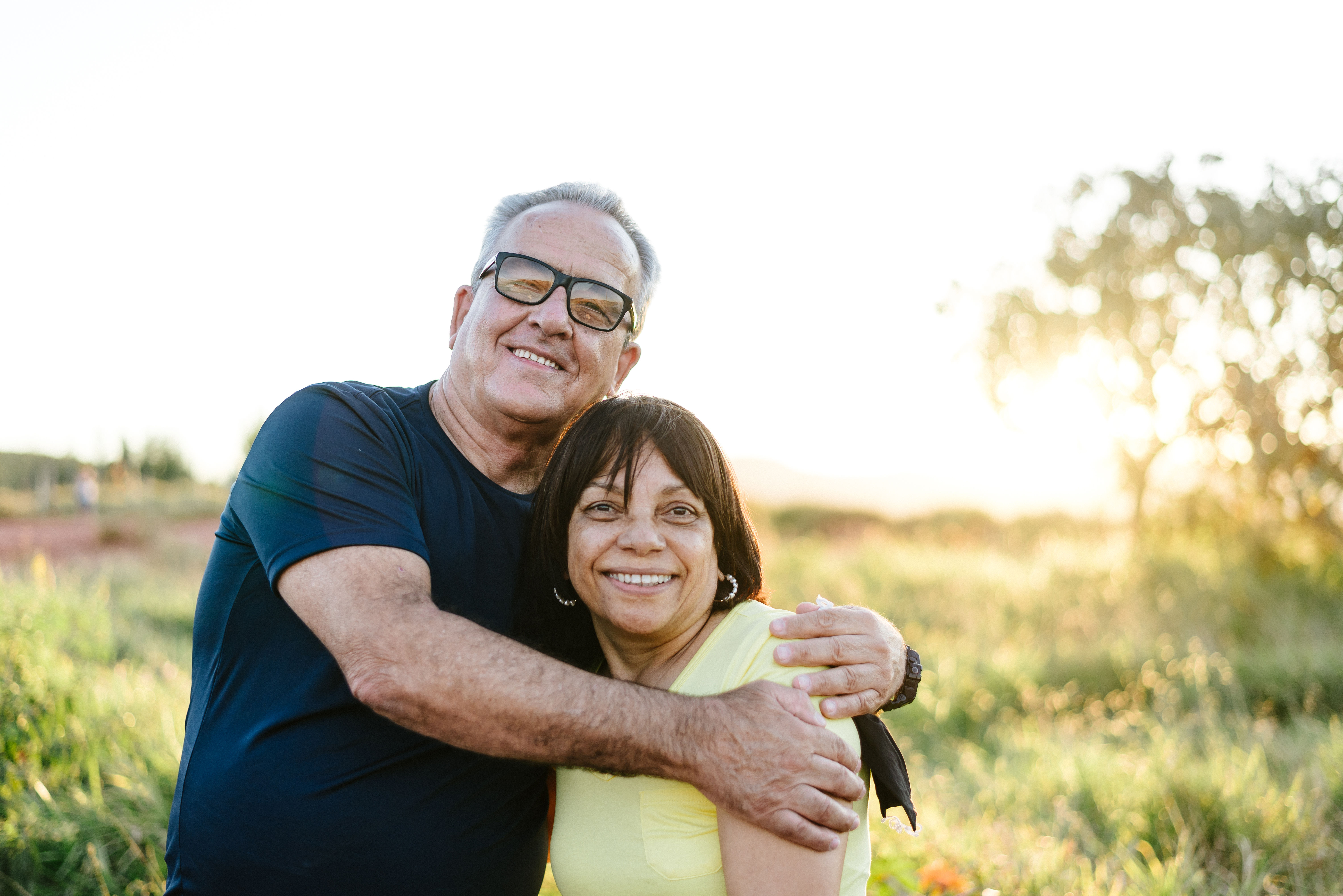 Two people hugging while standing outside in a field.