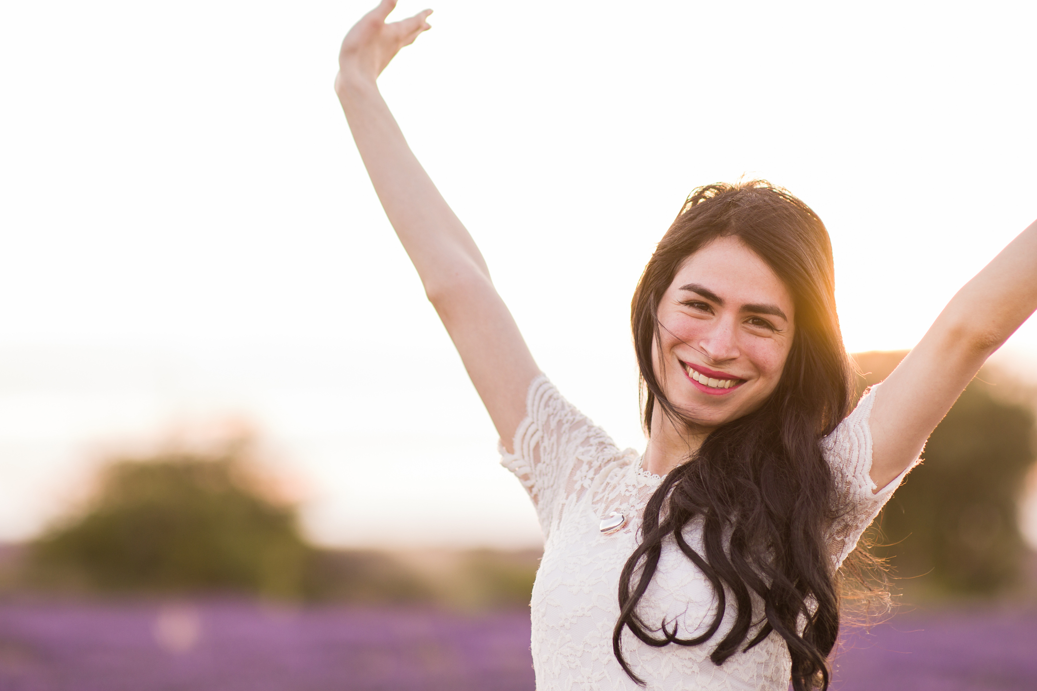 A person smiling outdoors, with arms outstretched.