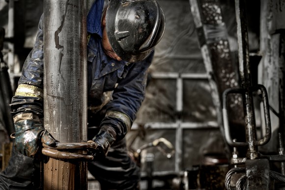 A person wearing personal protective equipment is covered with mud while working at a drilling site. 