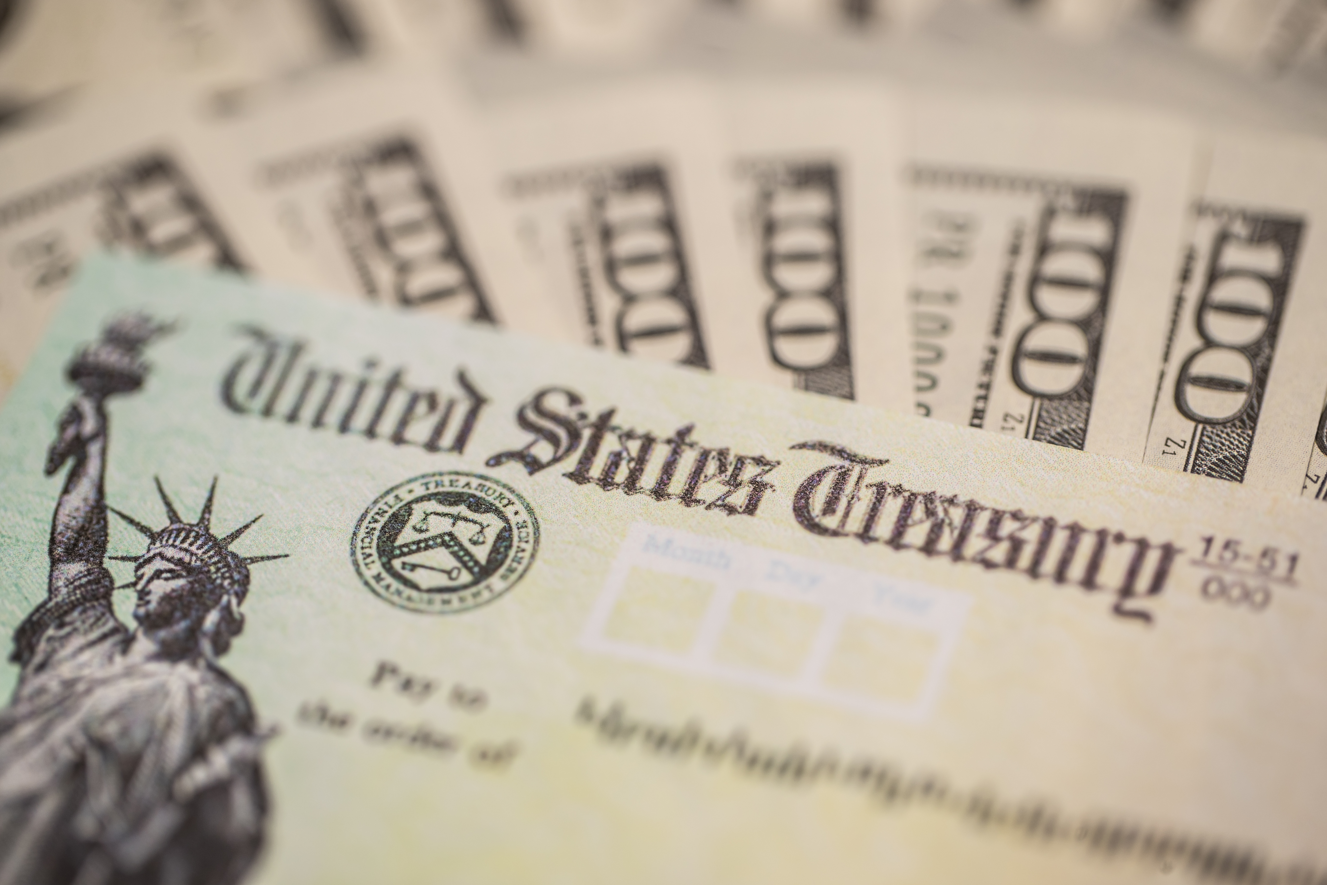 A U.S. Treasury check laying atop a fan of $100 bills.