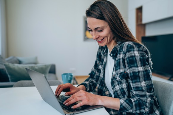 An investor smiles while working on a laptop at home.