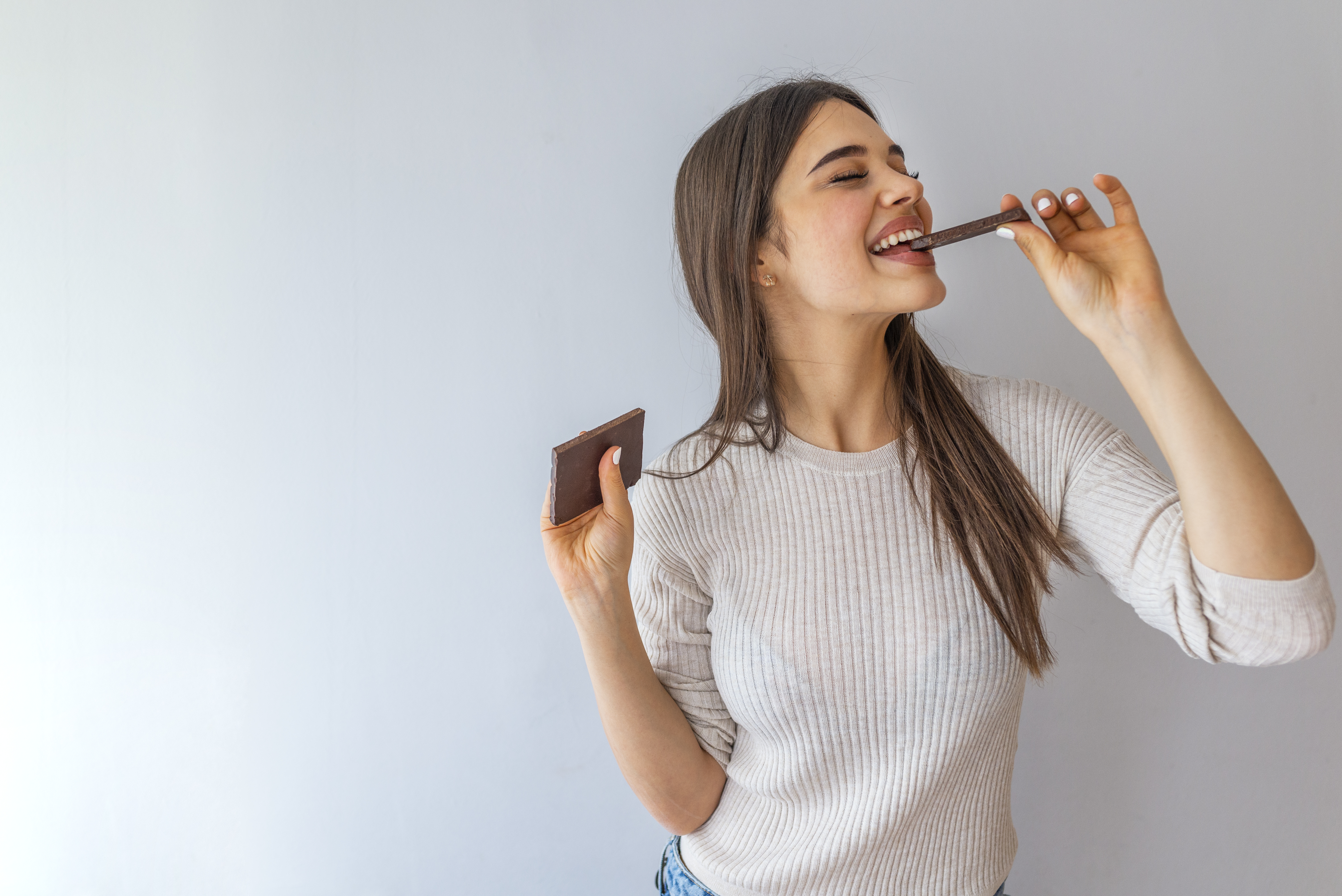 Person eating a chocolate bar while standing in front of a white backdrop.