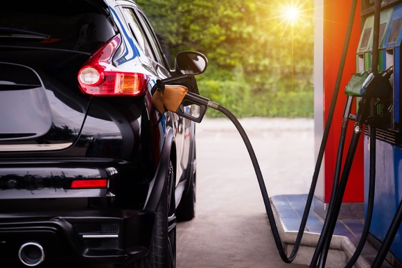 A black vehicle being refueled at a gas station, with a sunrise backdrop.