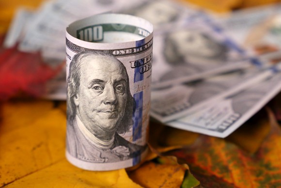 A rolled $100 bill in the foreground and fanned $100 bills in the background.