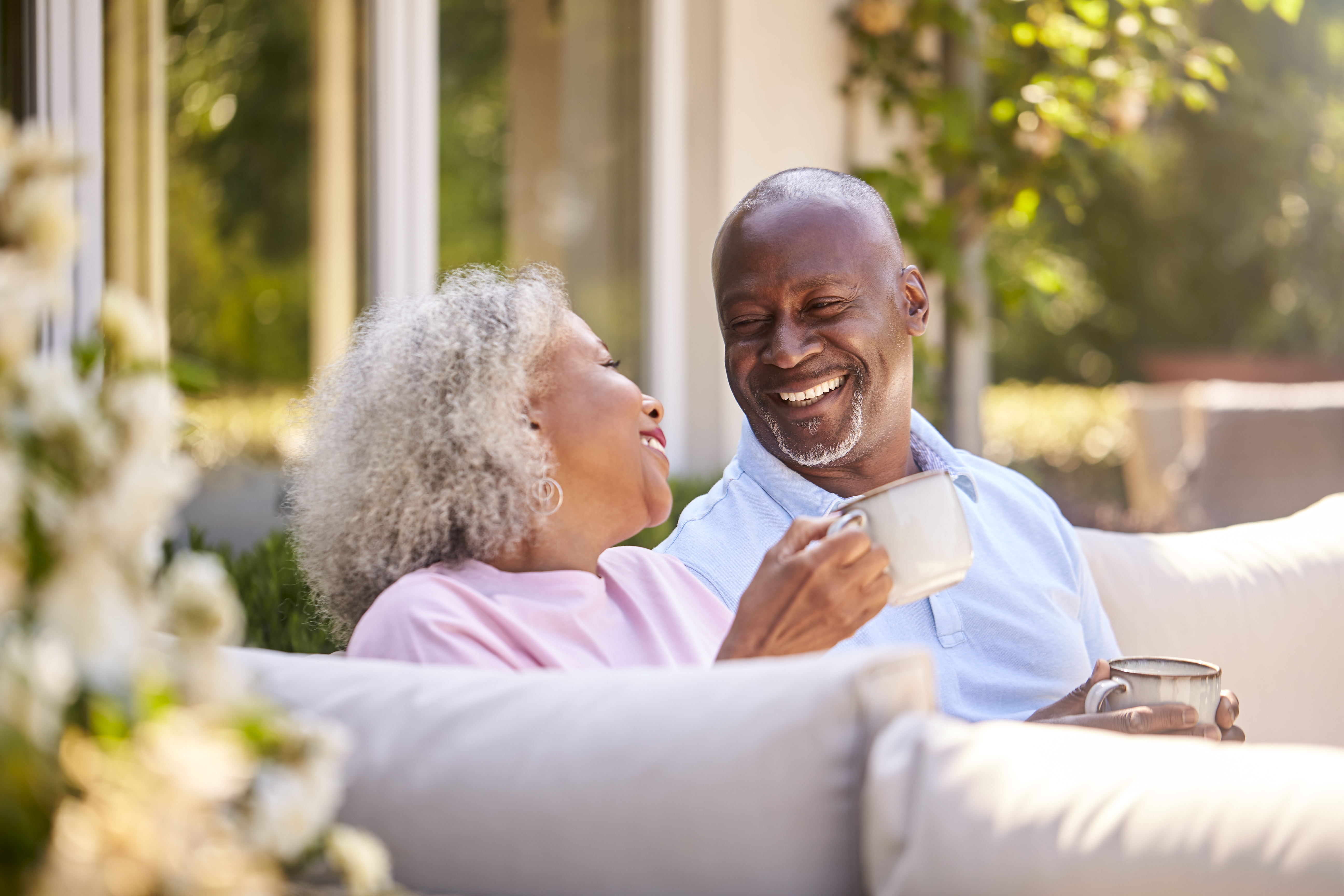 Two people sitting on a couch smiling and holding coffee mugs.