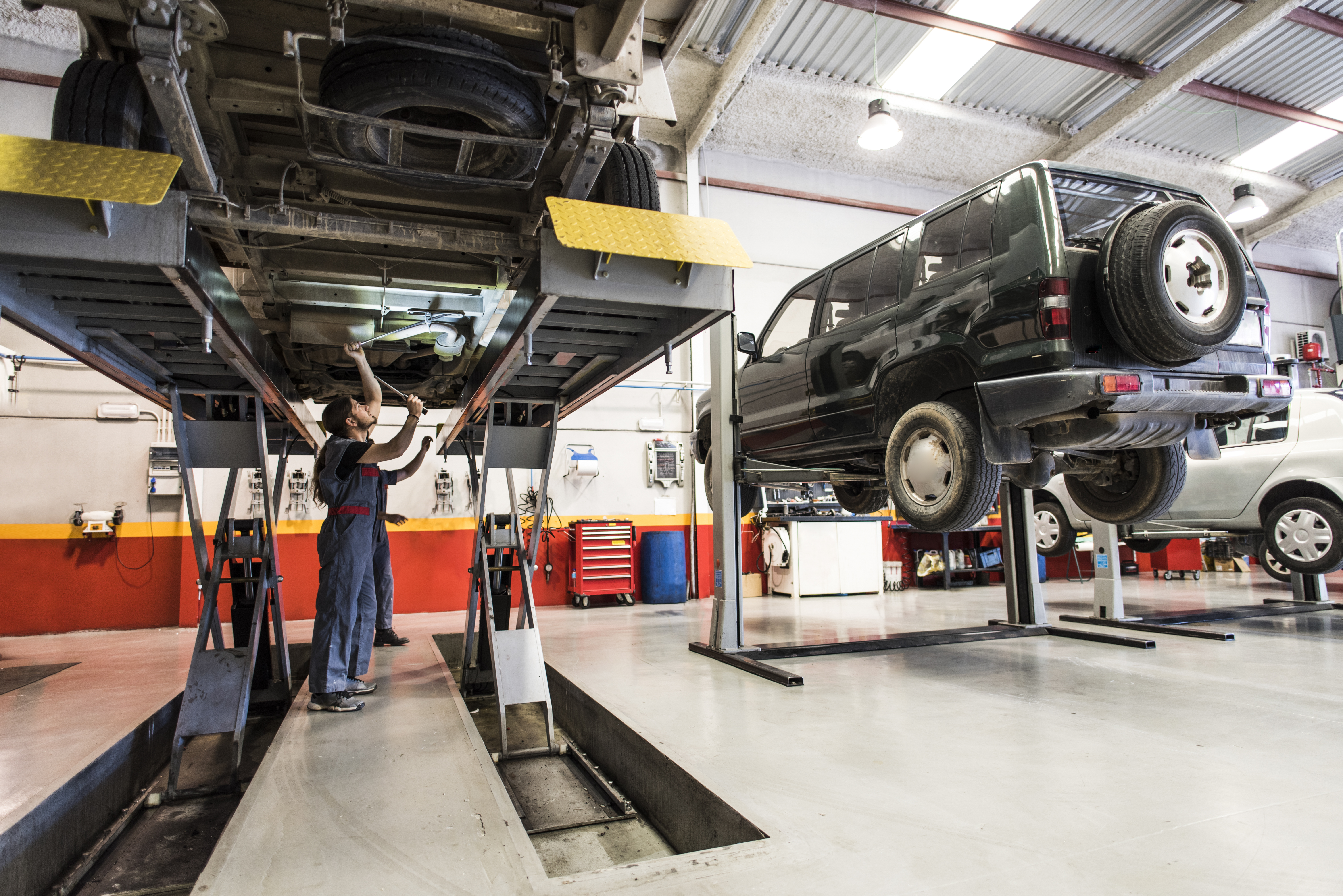 Mechanic works underneath a vehicle while it is on a lift in a repair shop.