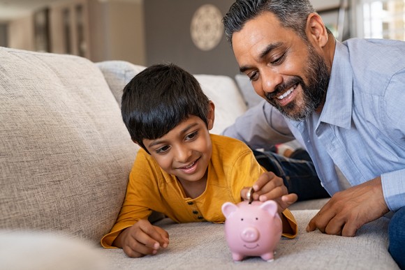 Parent teaching child about money by using piggy bank. 