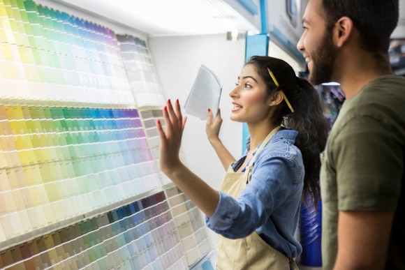 A person wearing an apron shows another person various color palettes. 
