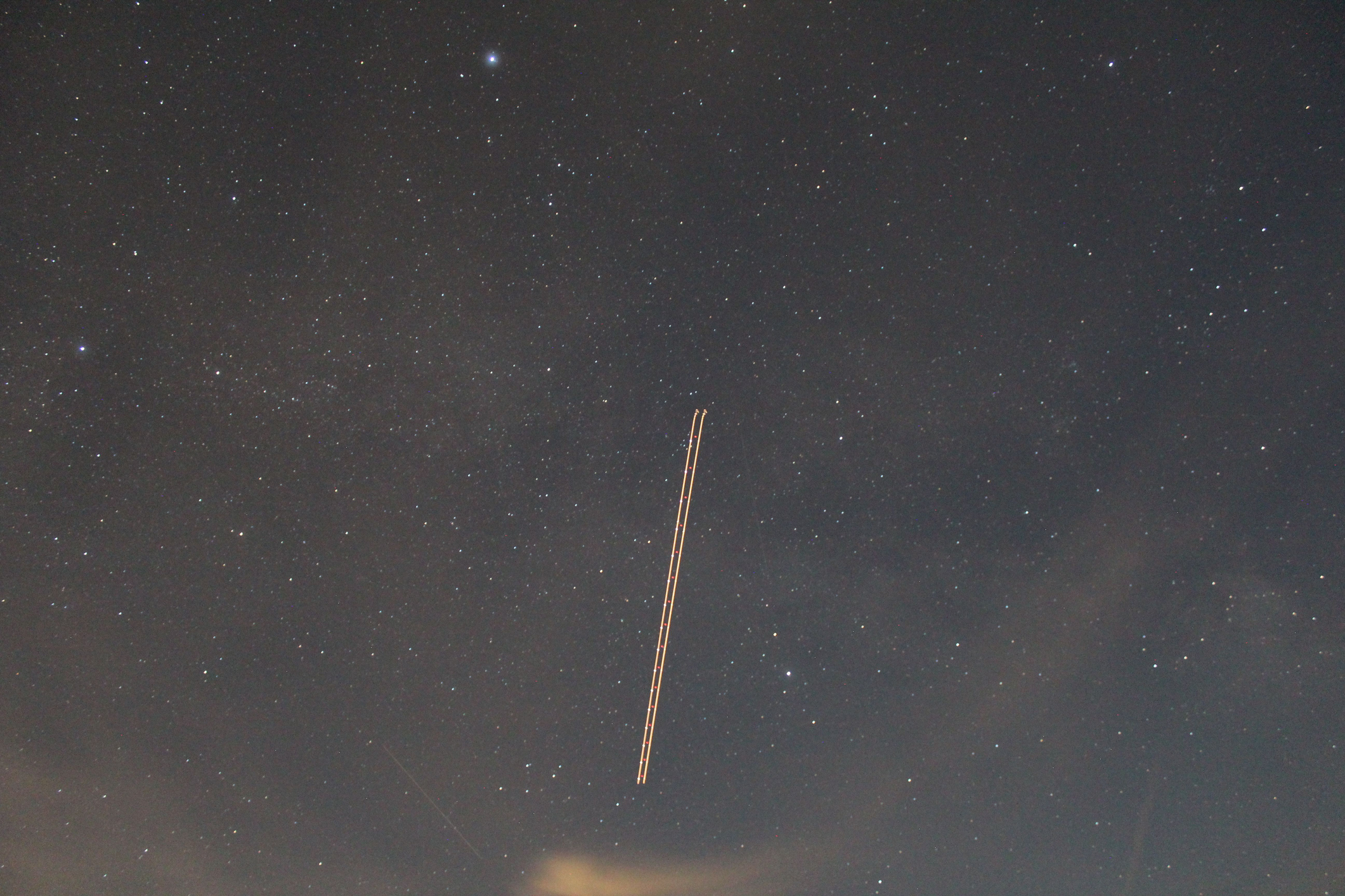 Long exposure photograph of a line of recently deployed Starlink satellites in the sky.