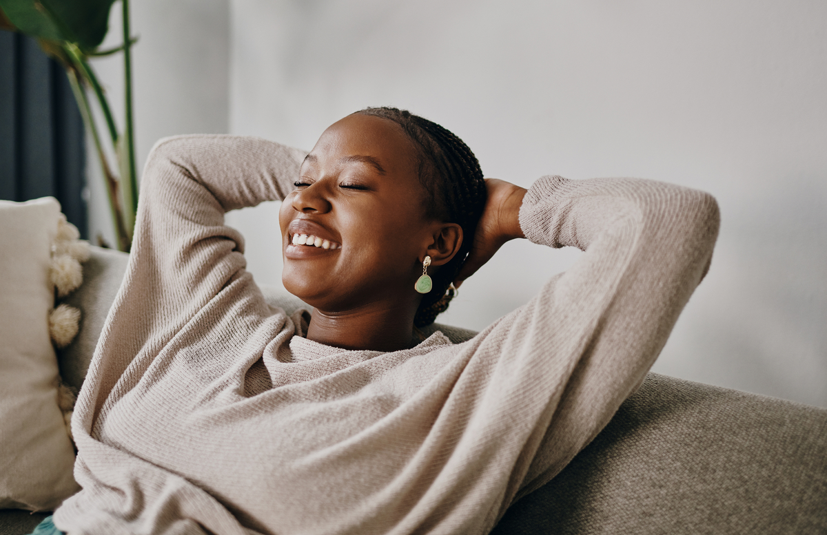 Relaxed person sitting on couch with hands behind head.