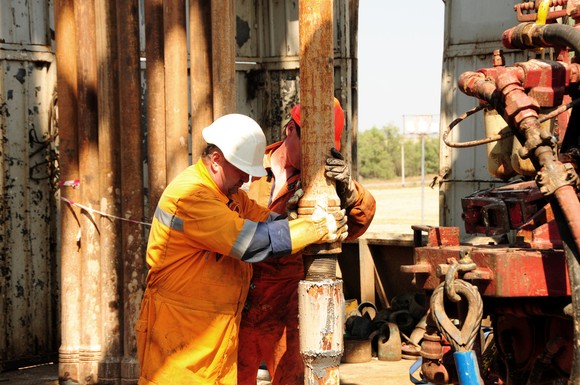 People wearing personal protective equipment are covered in mud as they work on a drilling rig. 
