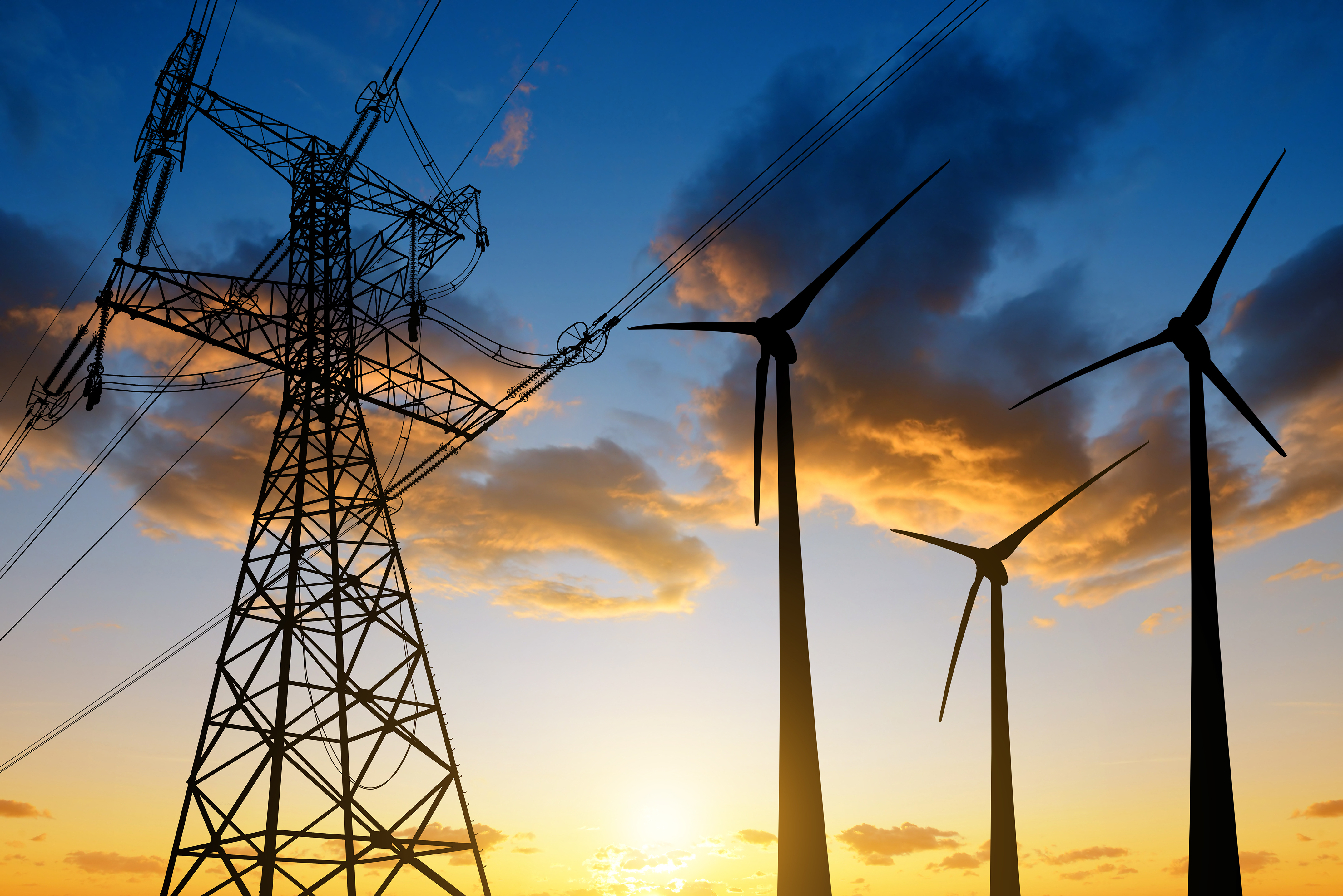 Three wind turbines next to a transmission tower, with the sun rising in the background.