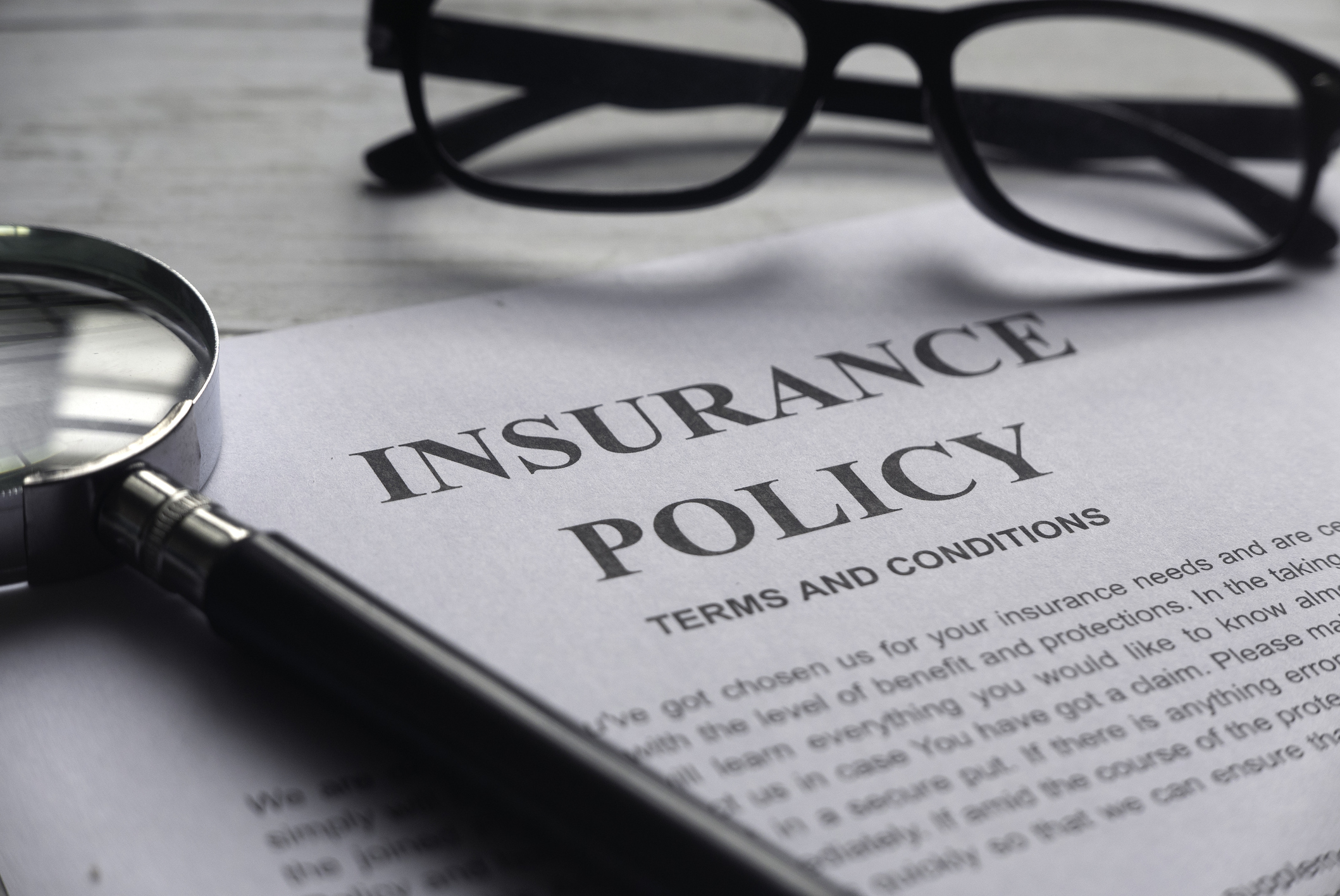 A magnifying glass and pair of glasses set atop paperwork displaying terms and conditions of an insurance policy.