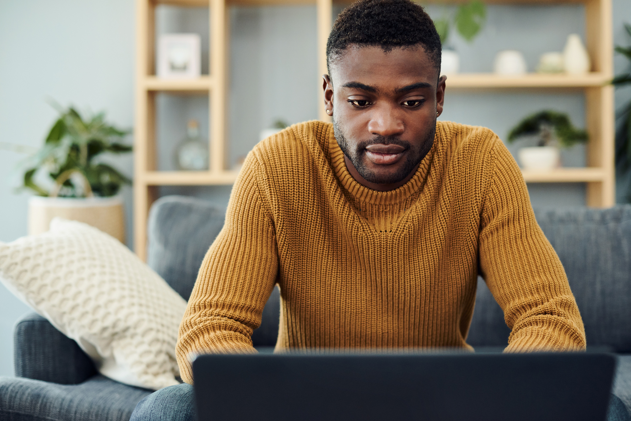 A person sitting on a couch who's typing on a laptop that's set on a tablet in front of them.