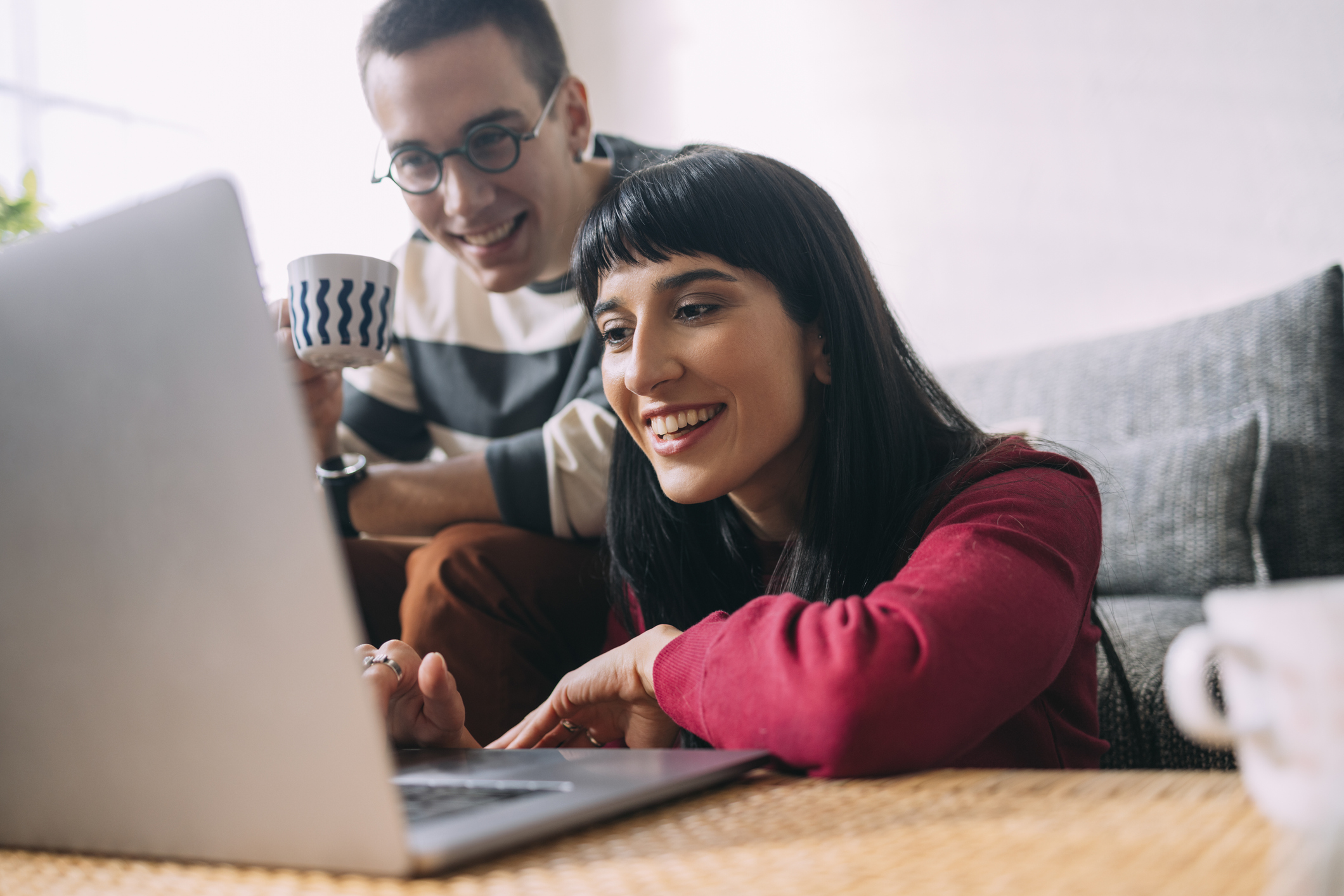 Two investors in a living room smile while looking at something on a laptop.