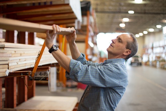 Person moving a piece of lumber off a shelf at a home improvement store.