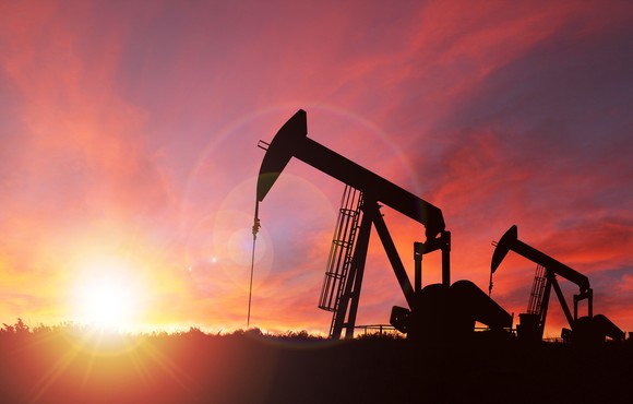 Silhouettes of two pumpjacks at sunset with a bright pink sky in the background. 