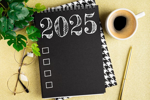 A notebook that reads "2025" with four unchecked boxes next to a plant, pair of glasses, cup of coffee, and a writing utensil. 