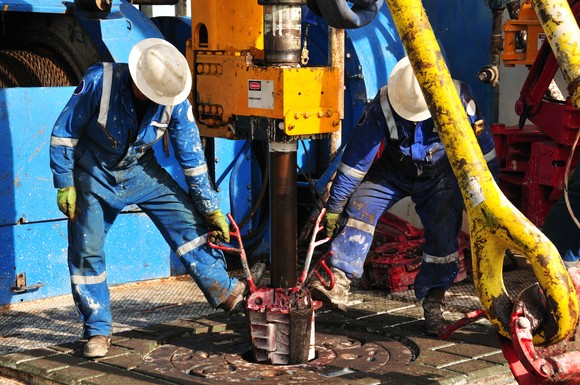 Oil rig employees aligning pipe and a drill. 