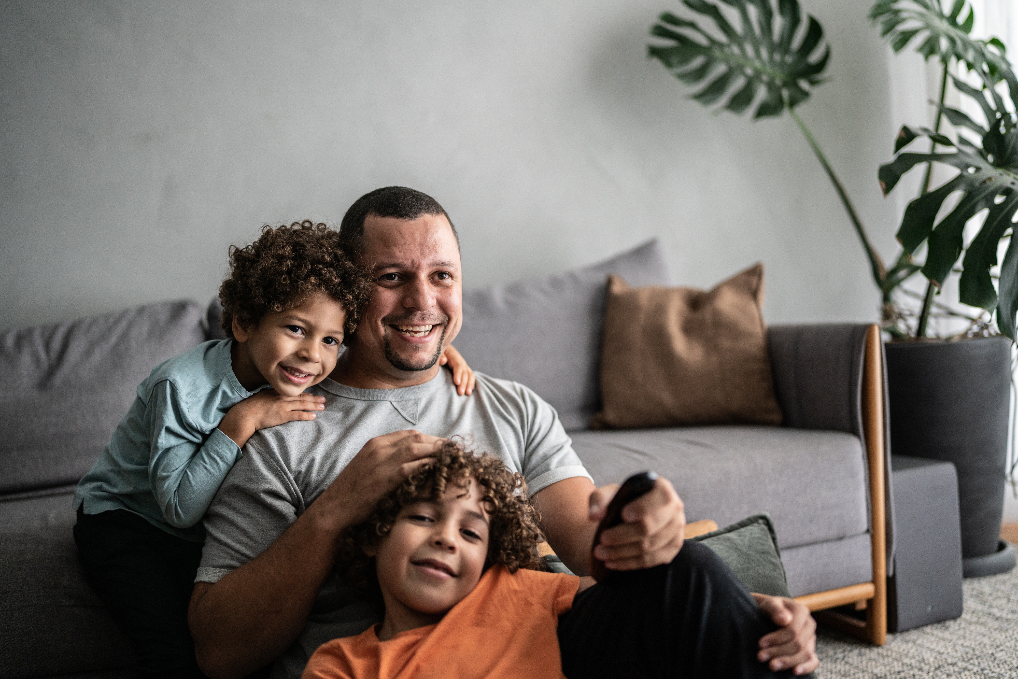 A parent sitting on the floor in front of a couch with their two children while watching television.