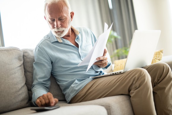 A person on a couch holding documents and using a calculator.