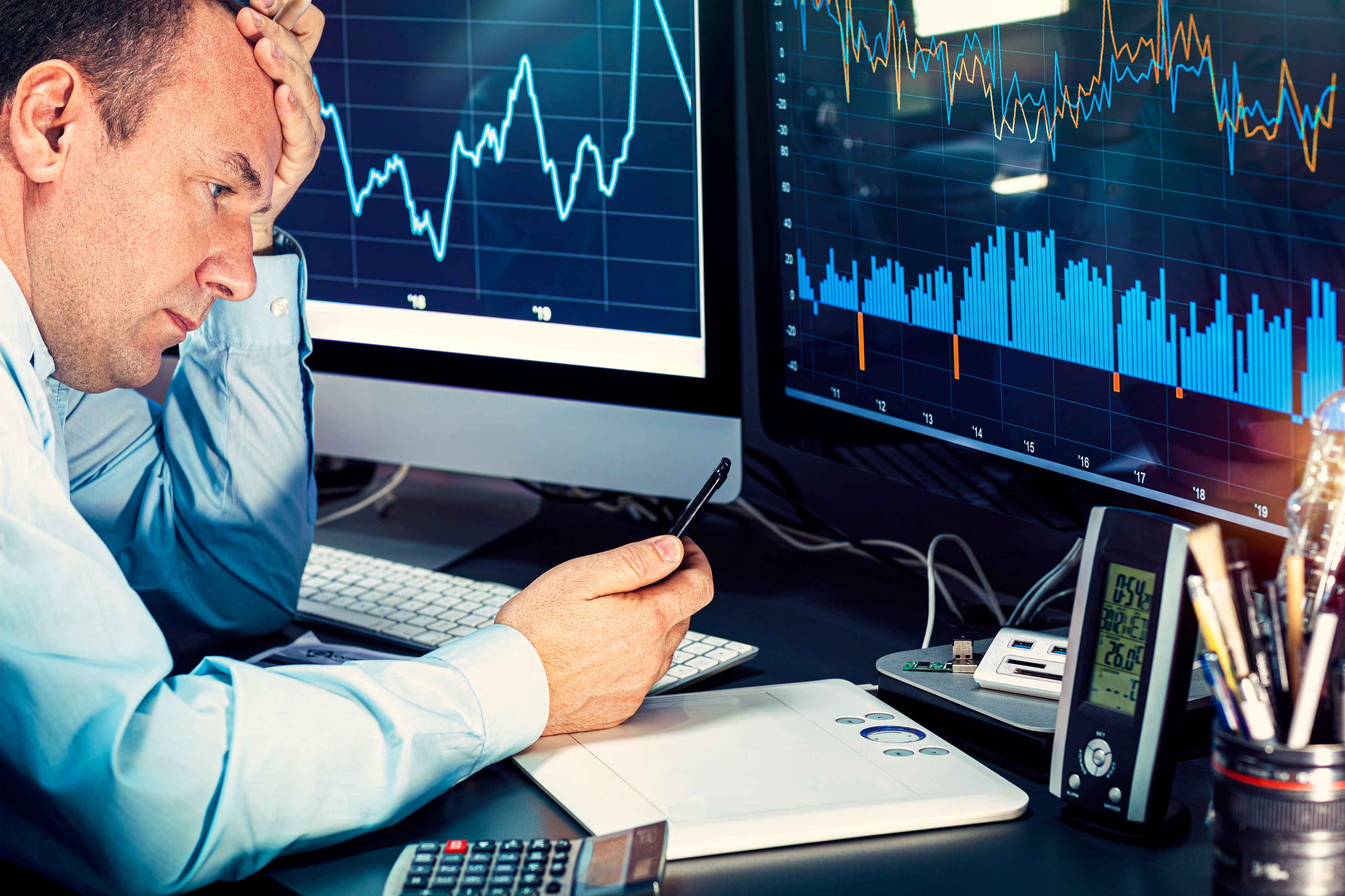 An analyst contemplating data displayed on two computer monitors.