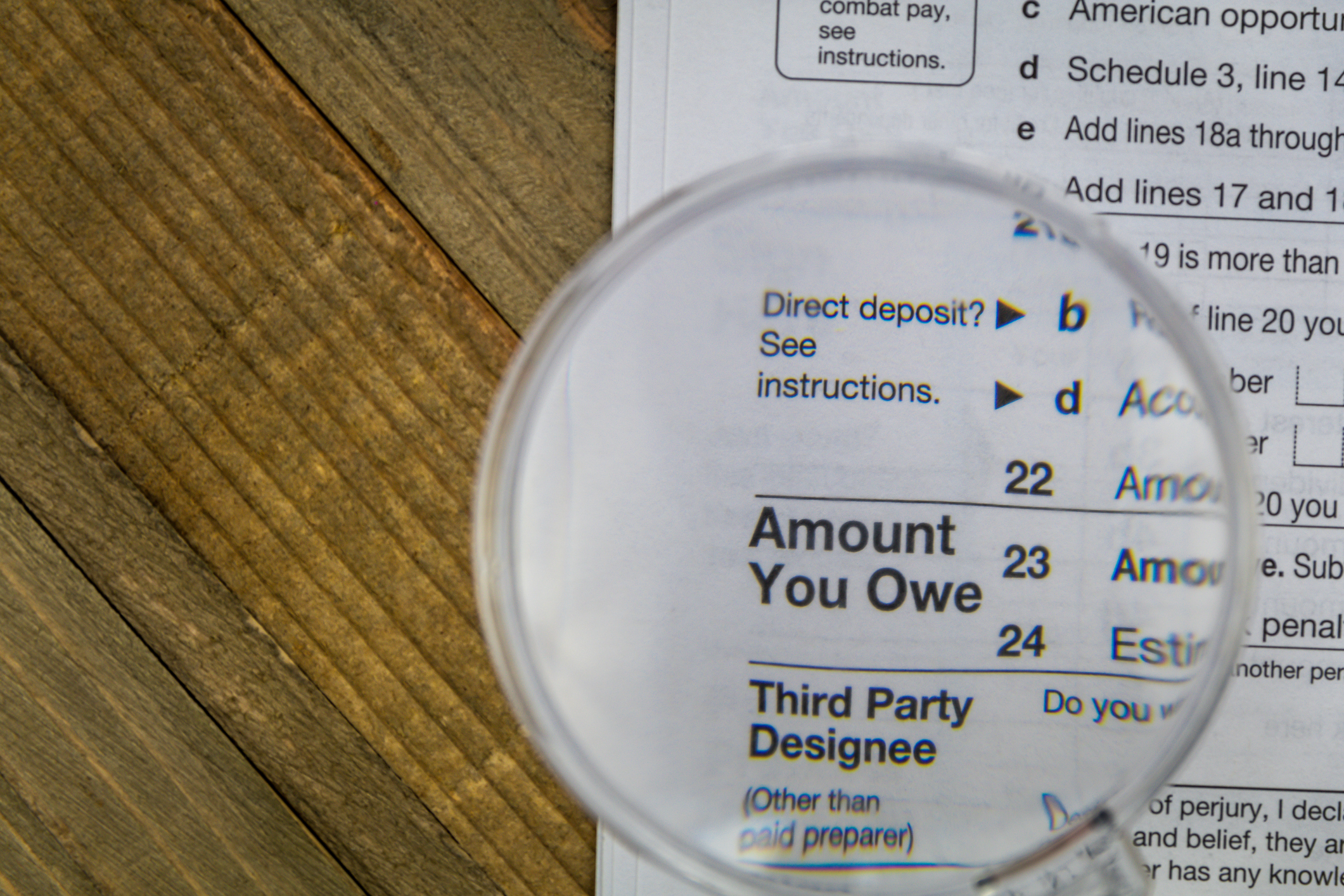 A magnifying glass set atop an IRS tax form, which is enlarging the phrase, Amount You Owe.