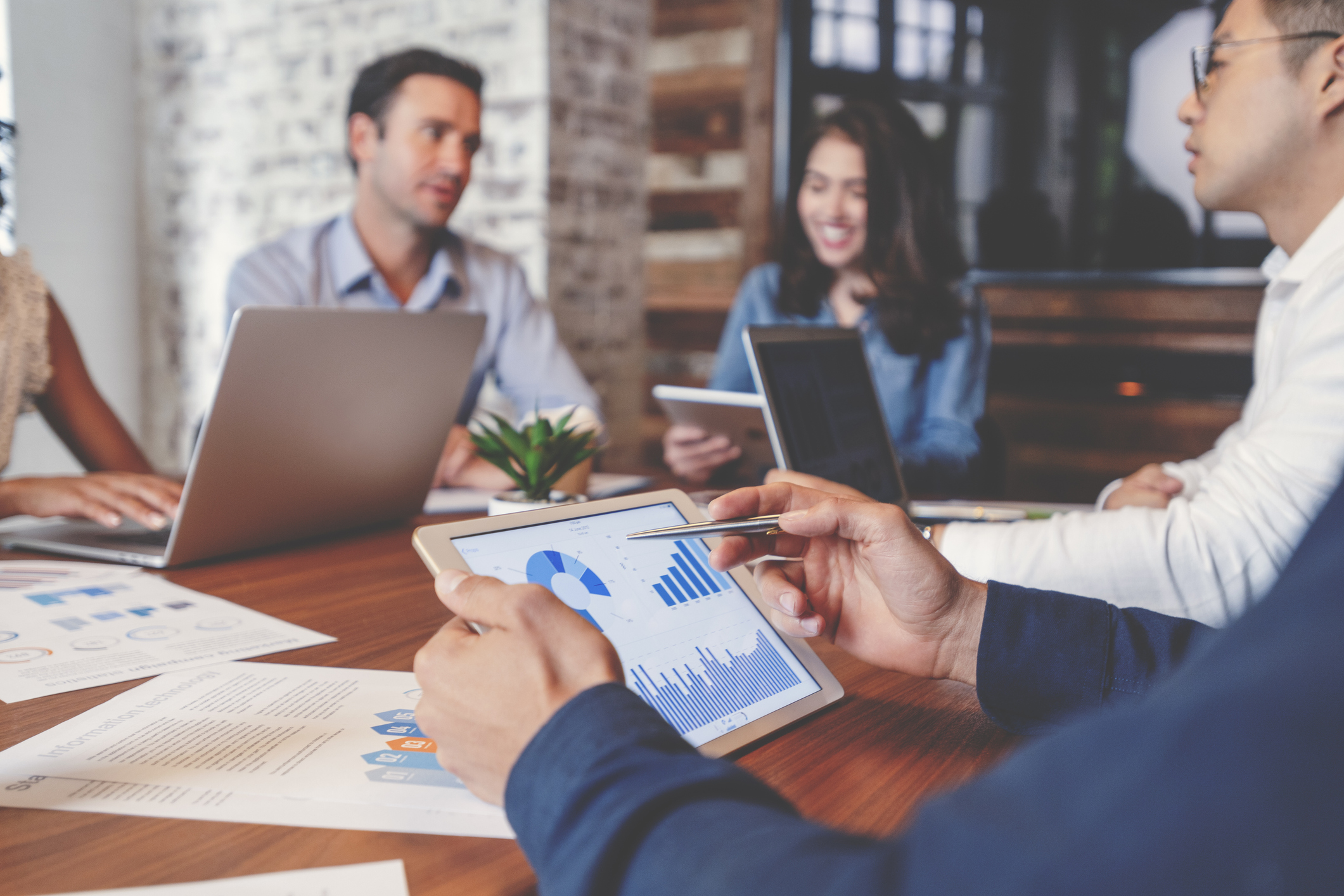 Employees using tablets and laptops to analyze business metrics while seated in a conference room.