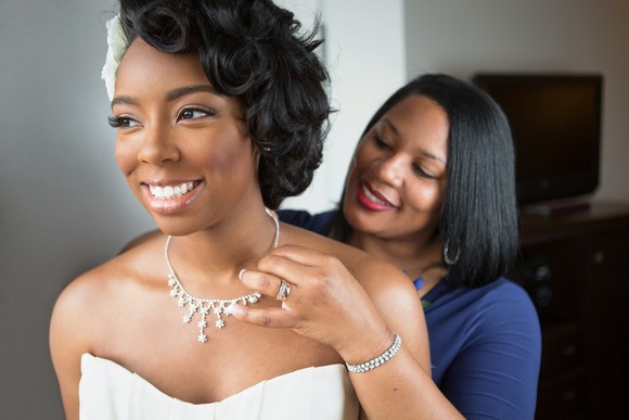 Person putting a necklace on a bride.