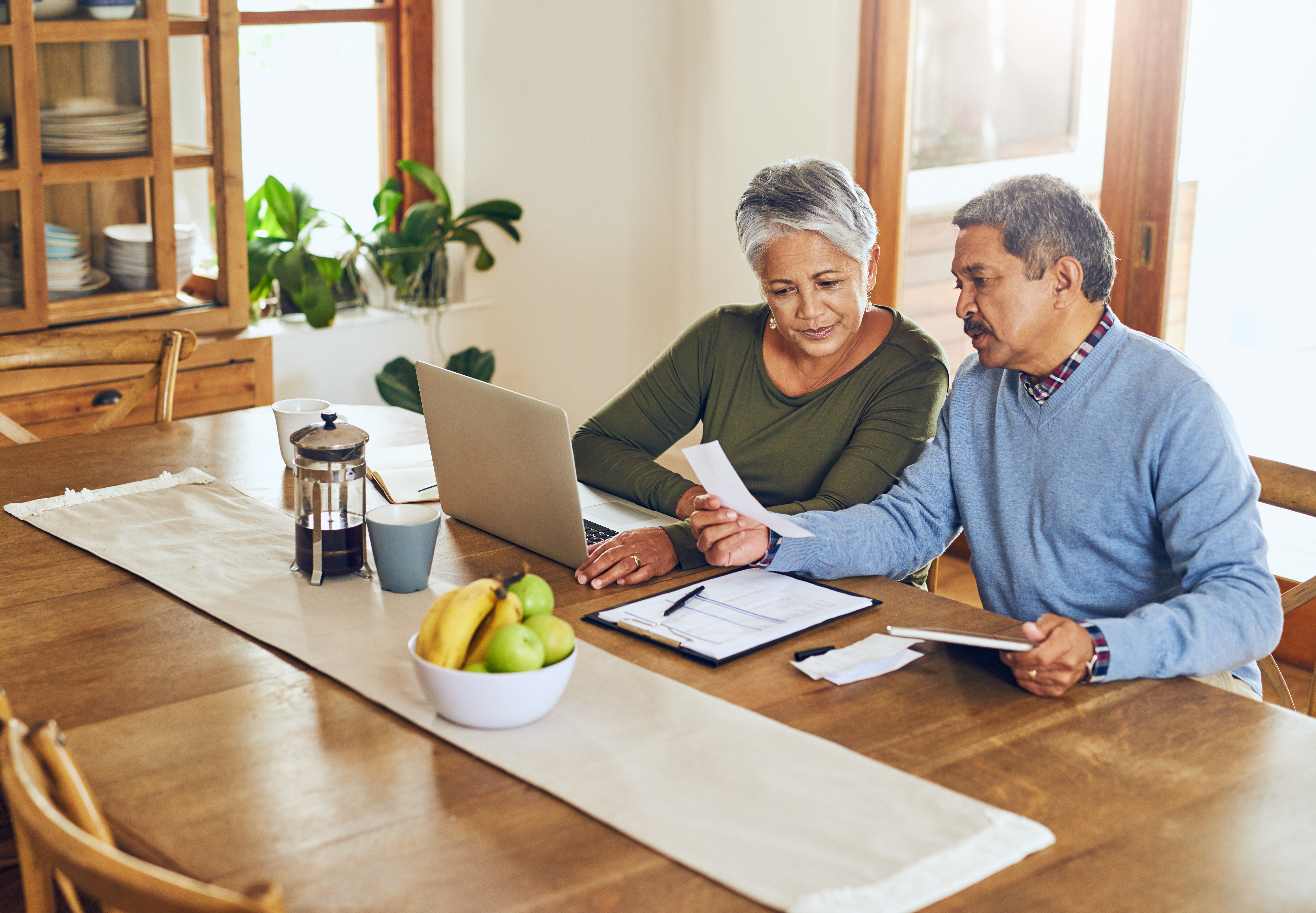 Two people sitting at table looking at computer and documents.