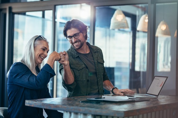 Two investors in an office bump fists and smile.