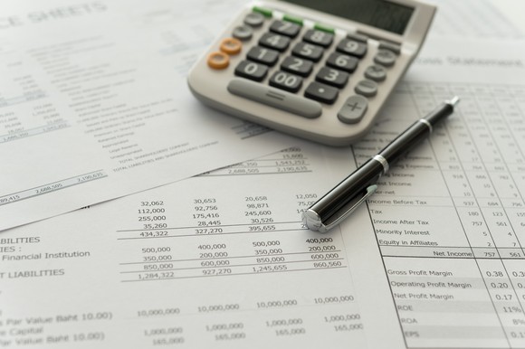 A calculator and pen set atop corporate income statements and balance sheets.